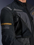 Alpinestars ST-7 2L GORE-TEX Jacket, Deep Gray and Black, close-up showing open zippered chest ventilation panel with mesh, Alpinestars logo on shoulder, and khaki stripe on the sleeve with printed geographic coordinates, technical adventure-touring motorcycle gear