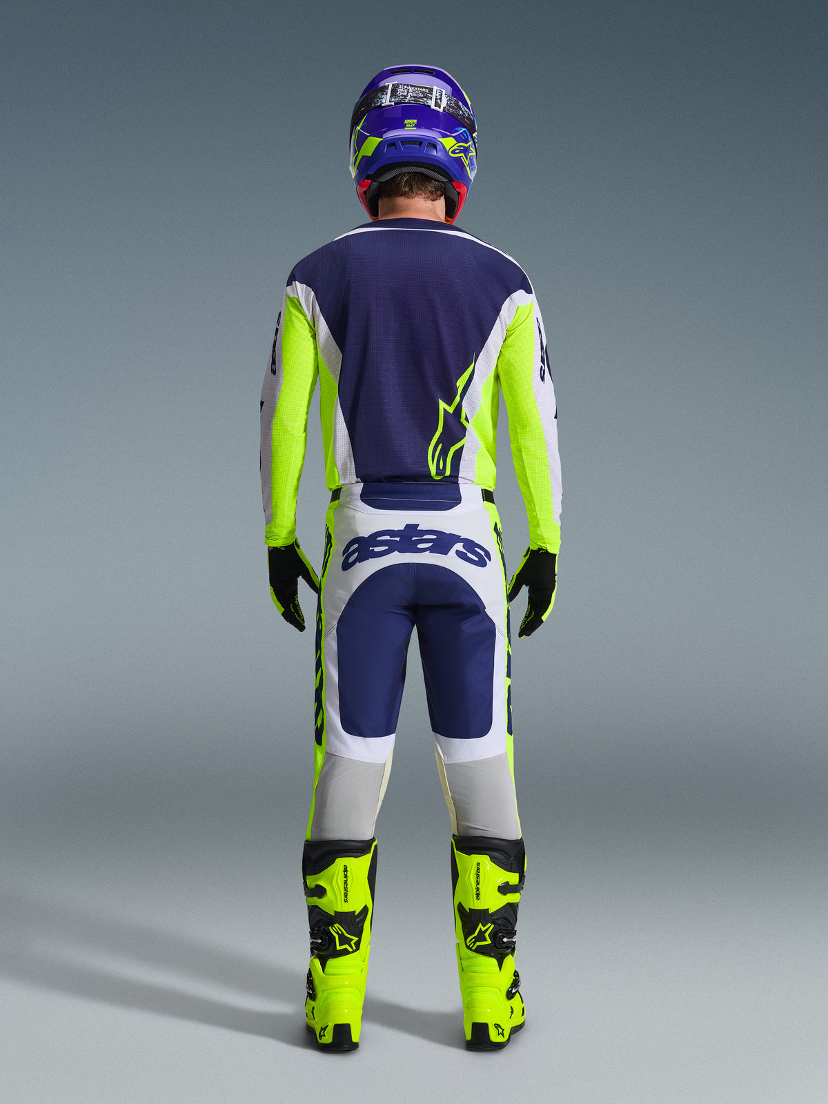 Motocross rider from the back wearing the Alpinestars 2026 Racer Air Riway Pants in Light Gray, Yellow Fluo, and Blue, paired with a matching jersey and bright yellow boots, illustrating a complete professional off-road racing gear set.