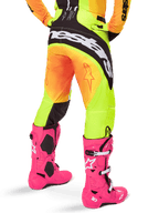 Rear view of a motocross rider wearing Alpinestars 2025 Techstar Melt Pants, Yellow and Orange gradient with black and white branding on the seat, paired with bright pink motocross boots, performance off-road gear.