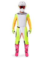 Motocross rider wearing the Alpinestars 2025 Techstar Melt Gear Set, white jersey with yellow and orange sleeves, neon yellow pants with white and orange accents, white helmet with red goggles, bright pink boots, and neon yellow gloves, complete racing outfit for off-road competition