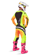 Motocross rider from behind wearing the Alpinestars 2025 Techstar Melt Gear Set, yellow and orange gradient jersey and pants with black panels, white helmet with red goggles, bright pink boots, coordinated racing outfit for off-road performance