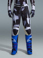 Alpinestars 2026 Racer Lahnd Pants, Motocross Pants, Iron Camo, worn with matching camouflage gloves and bright blue and purple boots, featuring stylized white star graphics on a dark camo pattern, technical magnetic buckle closure, professional off-road racing gear.
