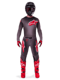 Motocross rider wearing complete Alpinestars 2025 Supertech Lipan gear set, Smoke Bright Red, featuring a dark grey jersey and pants with prominent red logos, black helmet with goggles, red and black gloves, and vibrant red motocross boots, coordinated professional racing outfit