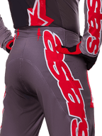 Alpinestars 2025 Supertech Lipan Pants, Motocross Pants, Smoke Bright Red, rear close-up view showing dark gray fabric with bold red graphics, worn with matching red and black gloves and jersey, featuring ventilation perforations and ergonomic stitching for off-road performance