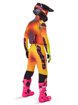Motocross rider from a rear view wearing Alpinestars 2025 Supertech Lipan Pants, Yellow and Pink gradient, styled with matching jersey, bright pink boots, and a black helmet with pink accents, professional coordinated outfit for off-road racing.