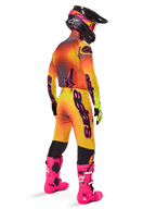 Motocross rider from a rear view wearing Alpinestars 2025 Supertech Lipan Pants, Yellow and Pink gradient, styled with matching jersey, bright pink boots, and a black helmet with pink accents, professional coordinated outfit for off-road racing.