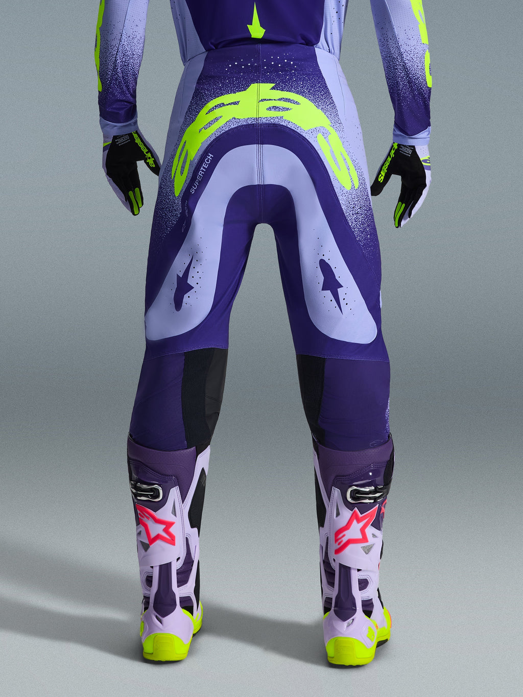 Alpinestars 2026 Supertech Scenz Pants, Motocross Pants, Purple and Yellow Fluo, rear view showing large yellow logo on seat, worn with matching jersey, gloves, and protective boots, athletic fit for professional motocross racing.
