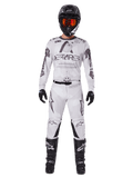Motocross rider wearing the Alpinestars 2025 Racer Hollow Pants in Light Camo Brown, paired with a matching white and grey long-sleeve jersey, black helmet with orange-red goggles, black gloves, and black boots, coordinated racing gear set for off-road performance.
