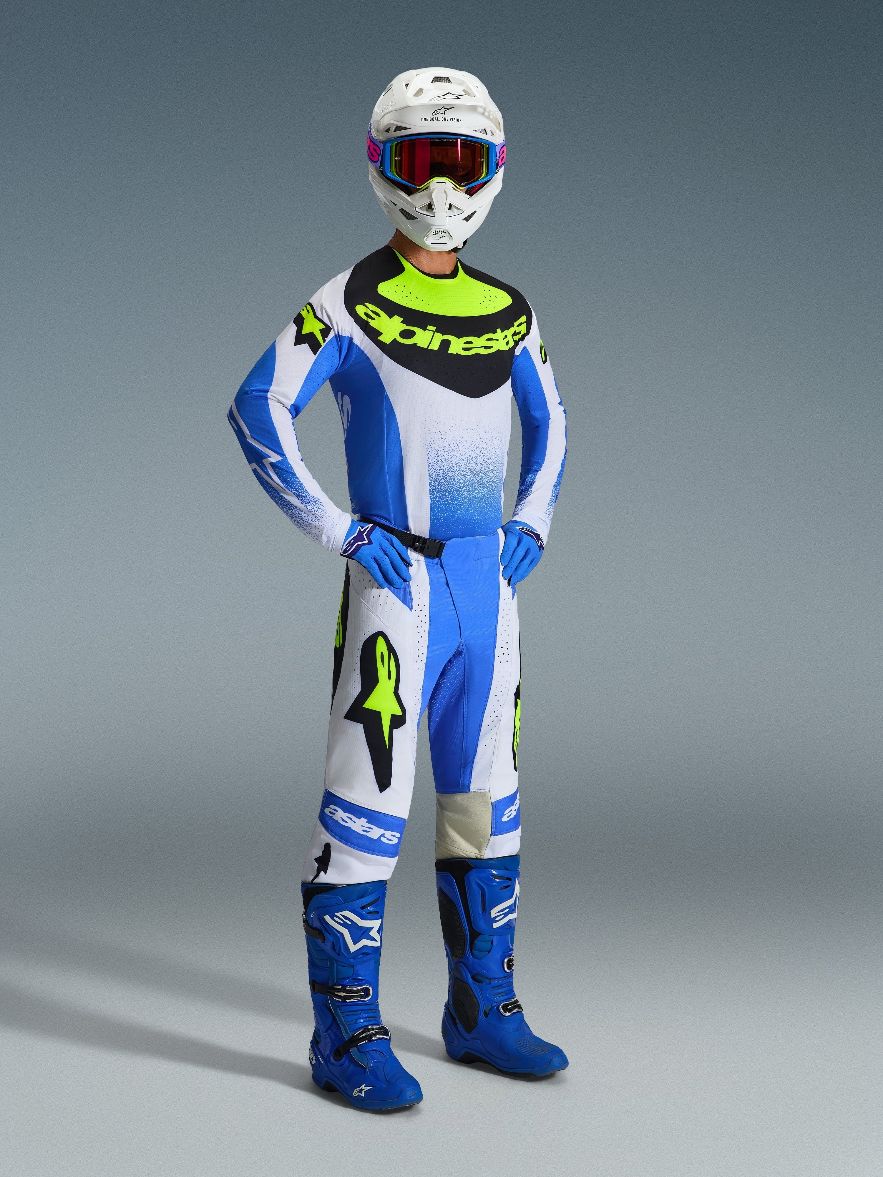 Motocross rider wearing Alpinestars 2026 Techstar Knif Pants in Ucla Blue, Black, and Yellow Fluo, full racing gear set with matching jersey featuring bold Alpinestars branding, blue boots, white helmet with goggles, and blue gloves, athletic stance for off-road performance