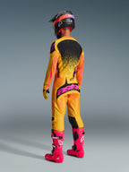 Motocross rider viewed from the back wearing complete racing gear, 2026 Techstar Nomur Pants in Orange Yellow Pink, bold pink 'astars' branding on the seat, matching jersey, bright pink boots, and black helmet with pink accents, coordinated off-road competition outfit.