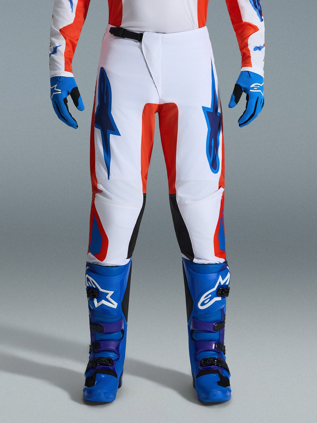 Alpinestars 2026 Fluid Grid Pants, Motocross Pants, Orange and UCLA Blue, worn with matching blue boots and gloves, featuring white chassis with bold blue logos and orange accents, ergonomic design for off-road performance