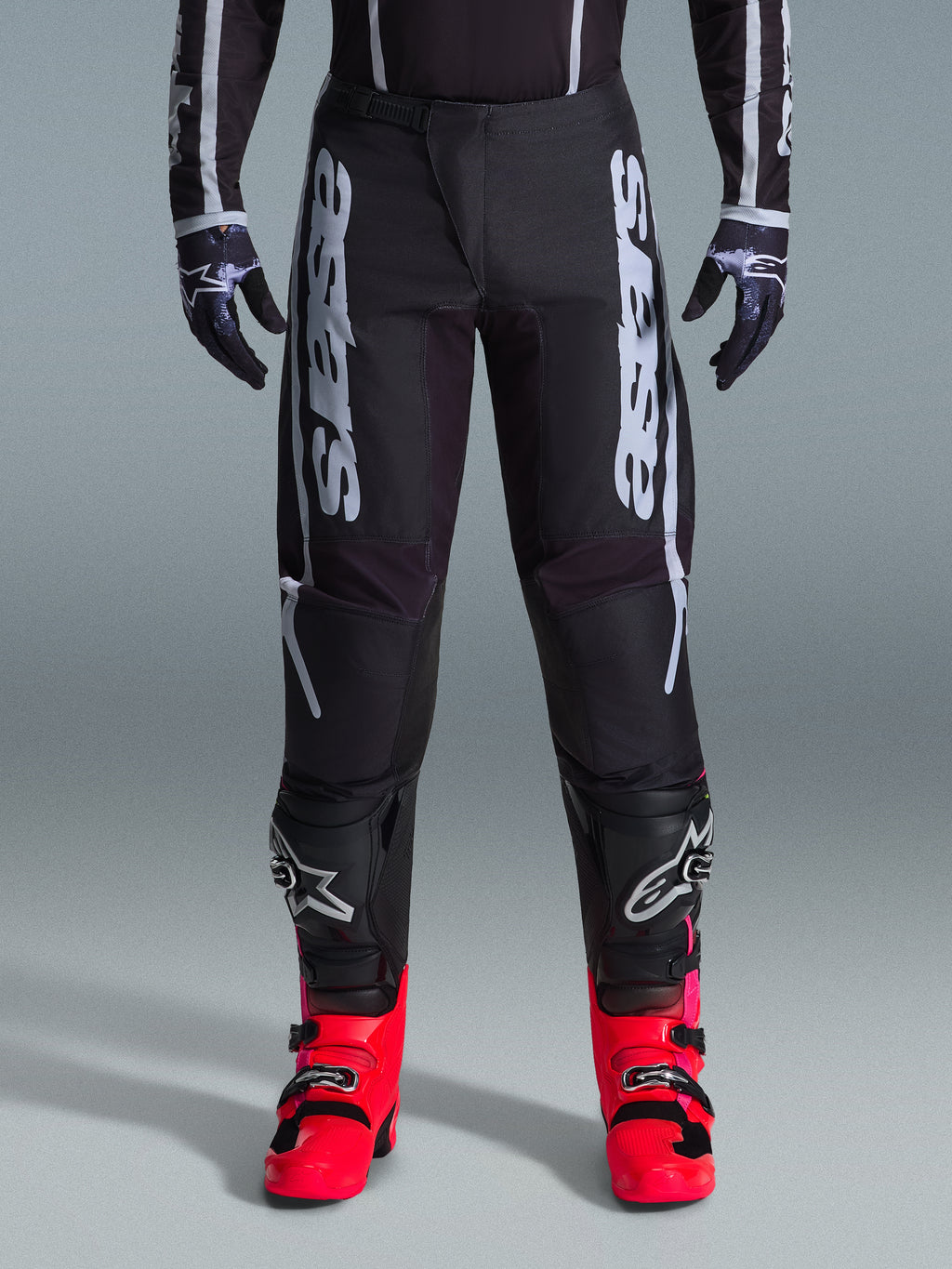 Alpinestars 2026 Fluid Apex Pants, Black Motocross Pants with large White Lettering, worn with black knee protection and vibrant red boots, lightweight 600D polyfabric chassis, sport-fit design for off-road racing