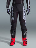 Alpinestars 2026 Fluid Apex Pants, Black Motocross Pants with large White Lettering, worn with black knee protection and vibrant red boots, lightweight 600D polyfabric chassis, sport-fit design for off-road racing