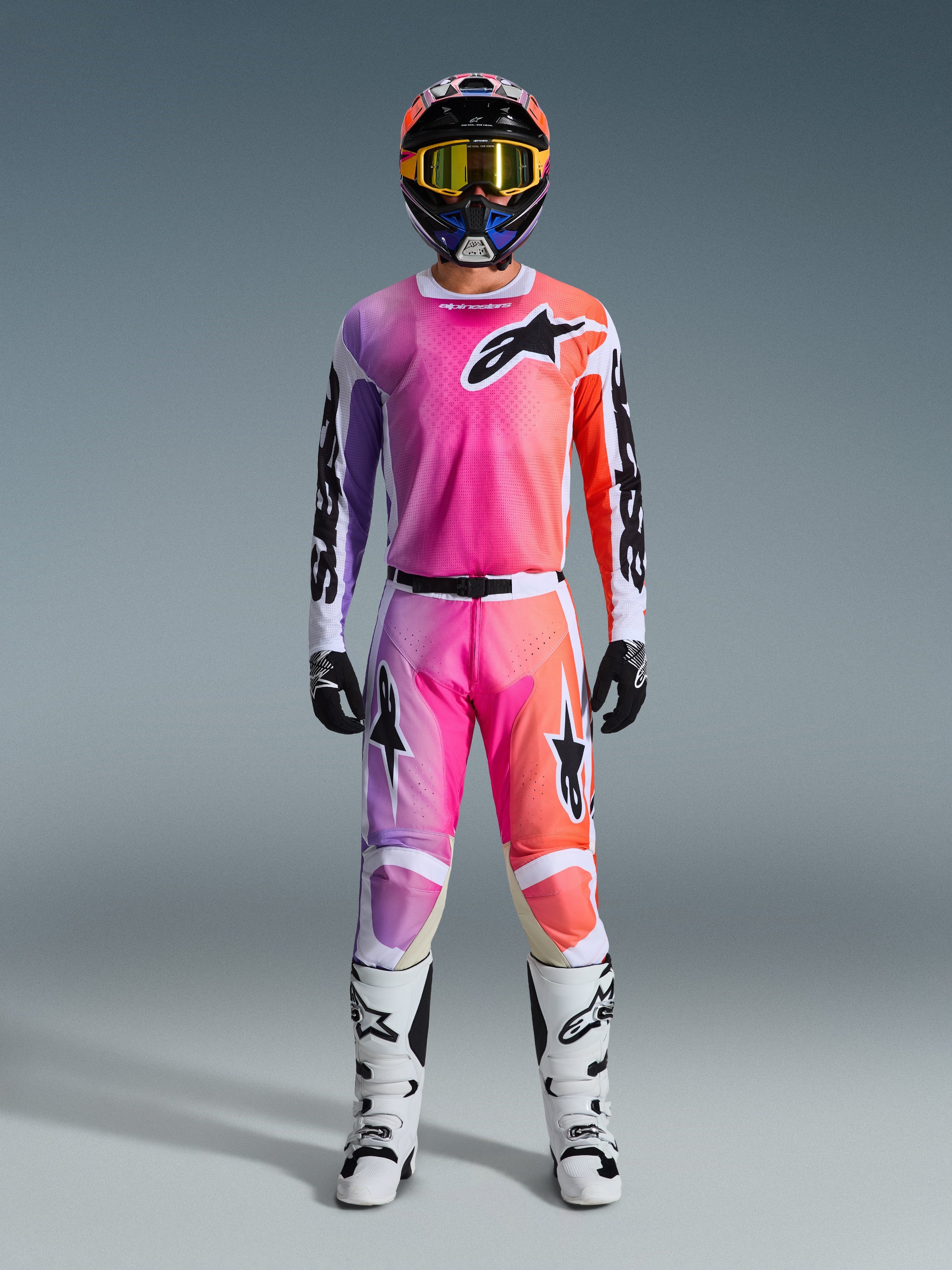 Motocross rider wearing the 2026 Racer Air Portl Jersey and matching pants, featuring a pink, purple, and orange gradient with black Alpinestars logos, white racing boots, black gloves, and a multicolor helmet, professional off-road racing gear.