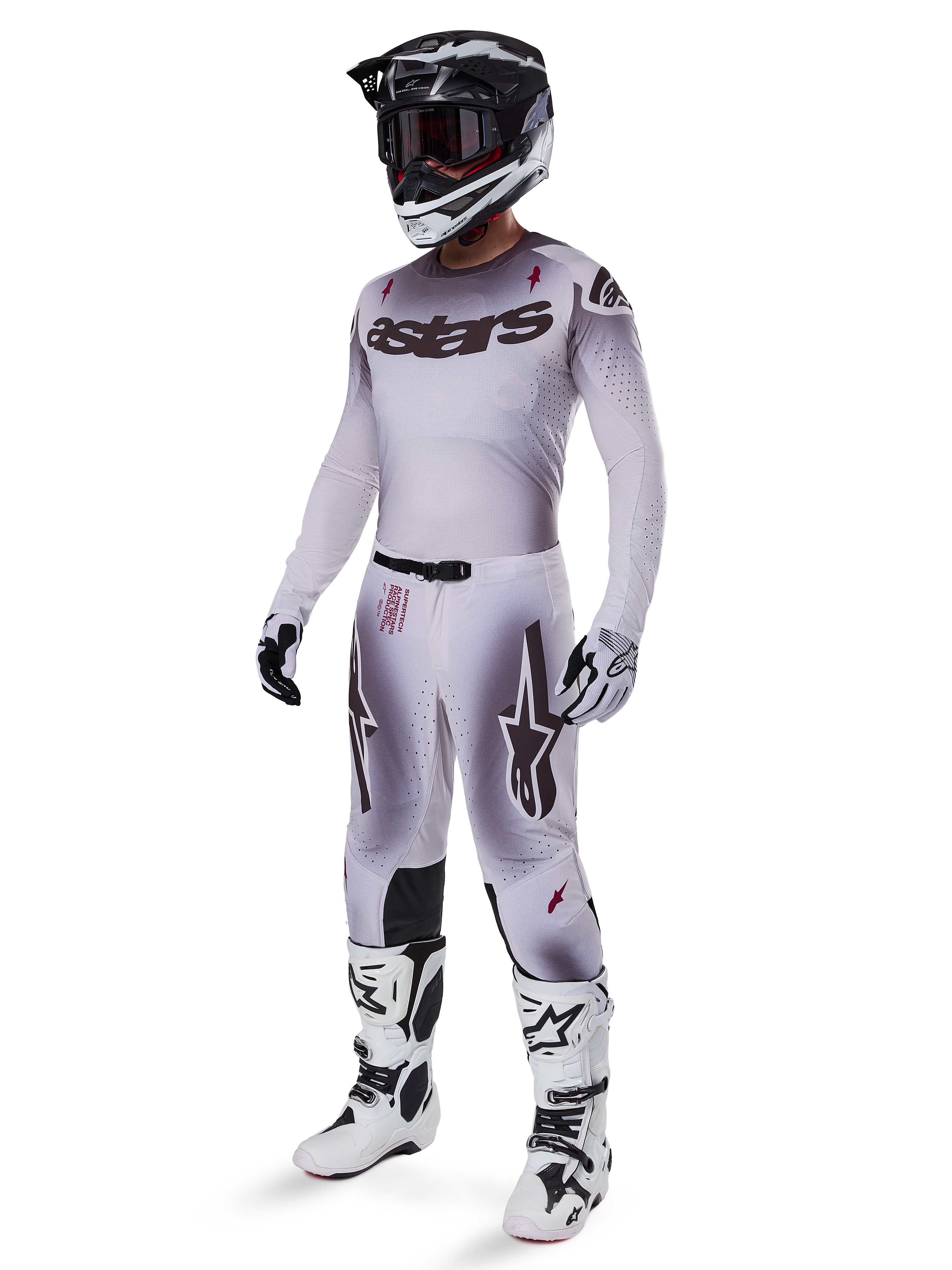 Motocross rider wearing the Alpinestars 2025 Supertech Maker Jersey in Silver and Black, matching silver and black pants, black and white helmet with black goggles, white and black boots, and coordinating gloves, professional gradient design for off-road racing