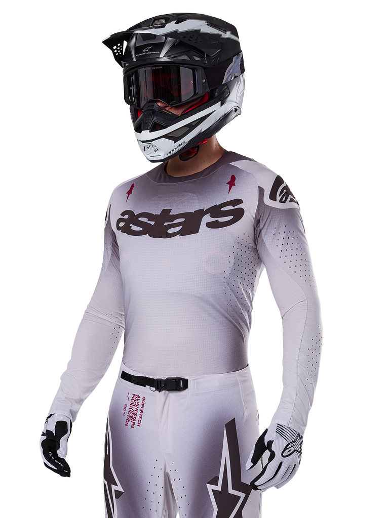 Alpinestars 2025 Supertech Maker Jersey, Motocross Racing Jersey, Silver and Black gradient, breathable stretch mesh with laser-cut perforations, worn with matching pants and helmet, featuring 'astars' branding, complete professional off-road gear