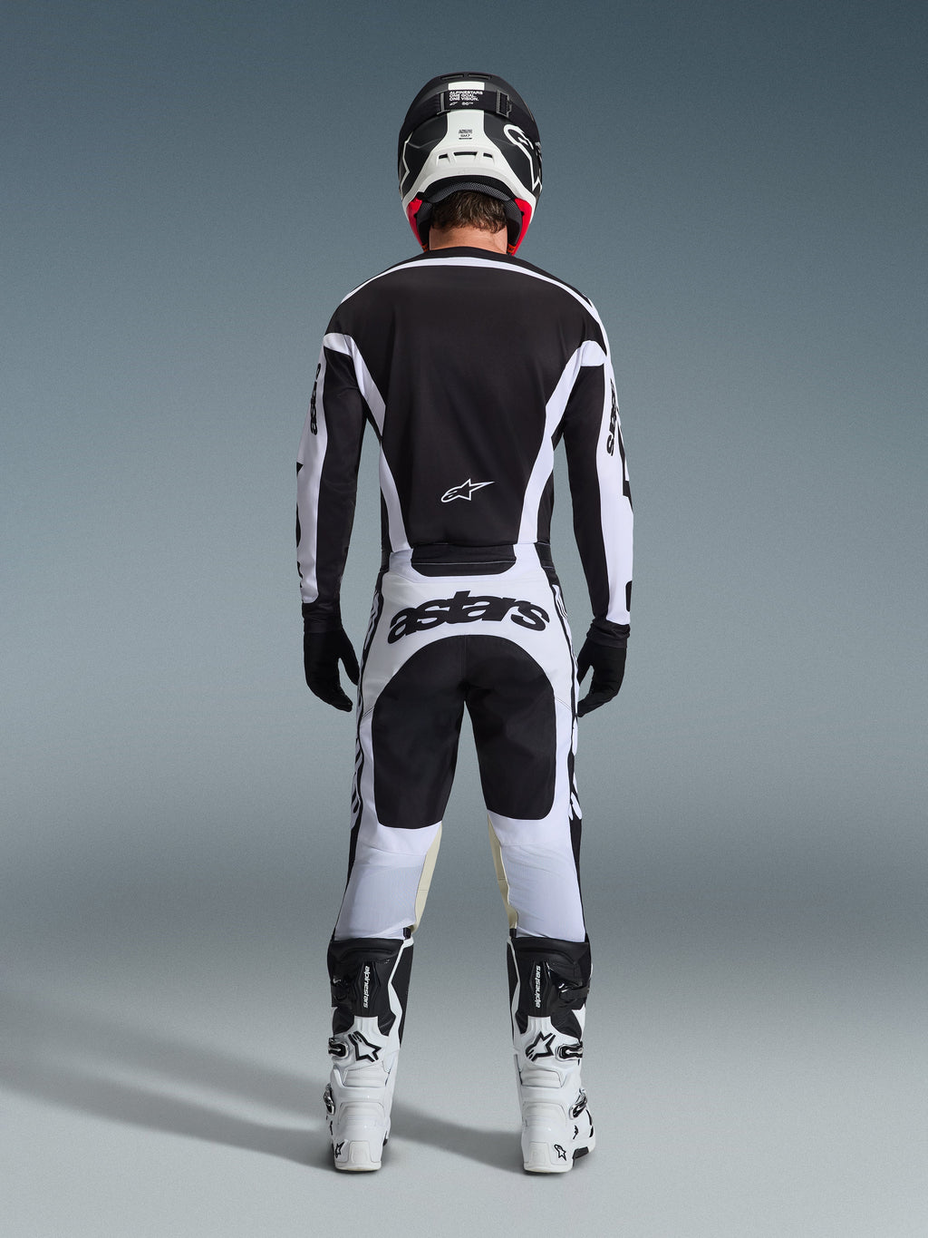 Motocross rider from the back wearing complete racing gear, 2026 Racer Riway Jersey in White and Black, matching pants with 'astars' branding on the seat, black helmet with white details, black gloves, and white and black boots, coordinated professional off-road outfit