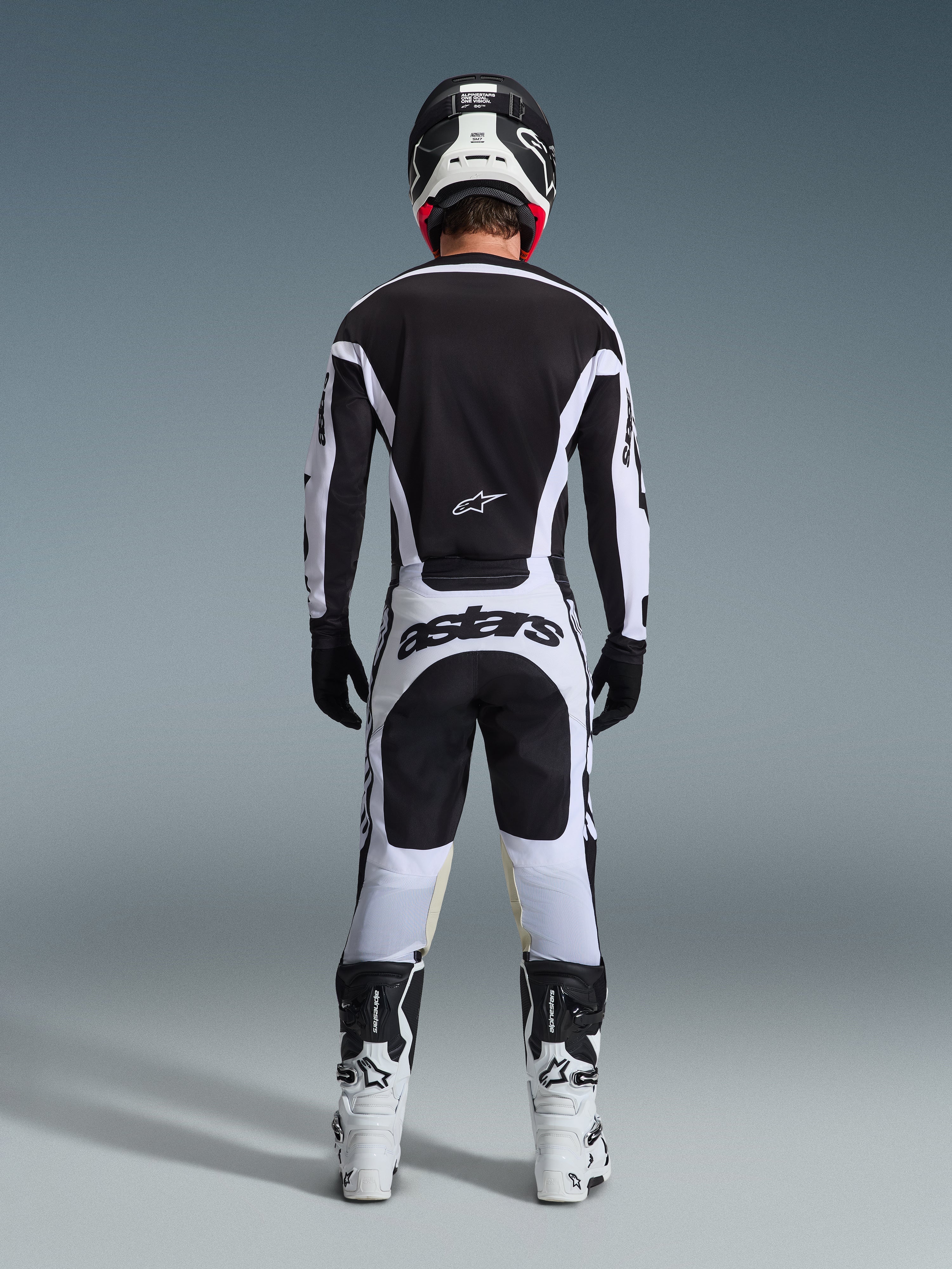 Motocross rider from the back wearing complete racing gear, 2026 Racer Riway Jersey in White and Black, matching pants with 'astars' branding on the seat, black helmet with white details, black gloves, and white and black boots, coordinated professional off-road outfit