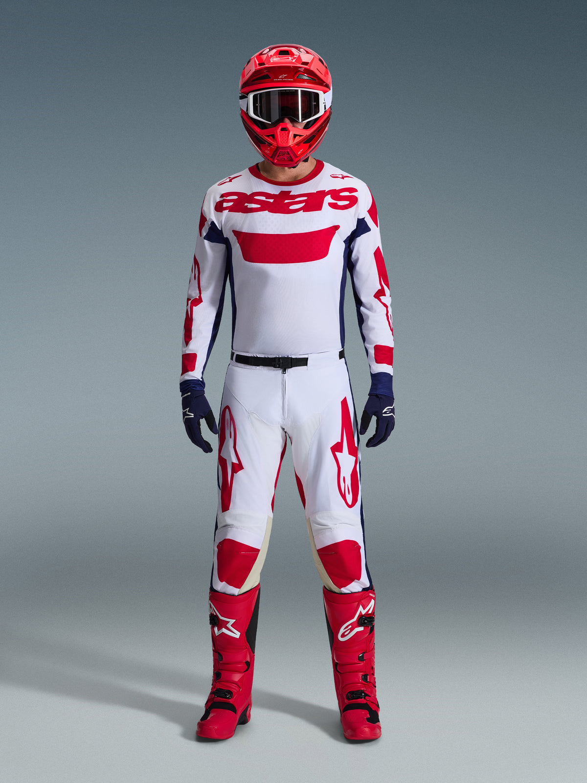 Motocross rider wearing complete racing gear, Alpinestars 2026 Racer Riway Jersey in White Blue Red, matching white and red pants, red helmet, red boots, and navy blue gloves, coordinated outfit for off-road racing