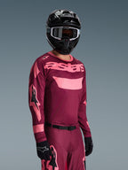 Motocross rider wearing Alpinestars 2026 Racer Riway Gear Set, Burgundy and Pink jersey with bold 'astars' branding, matching pants with pink accents, black helmet and gloves, professional racing outfit for off-road motocross