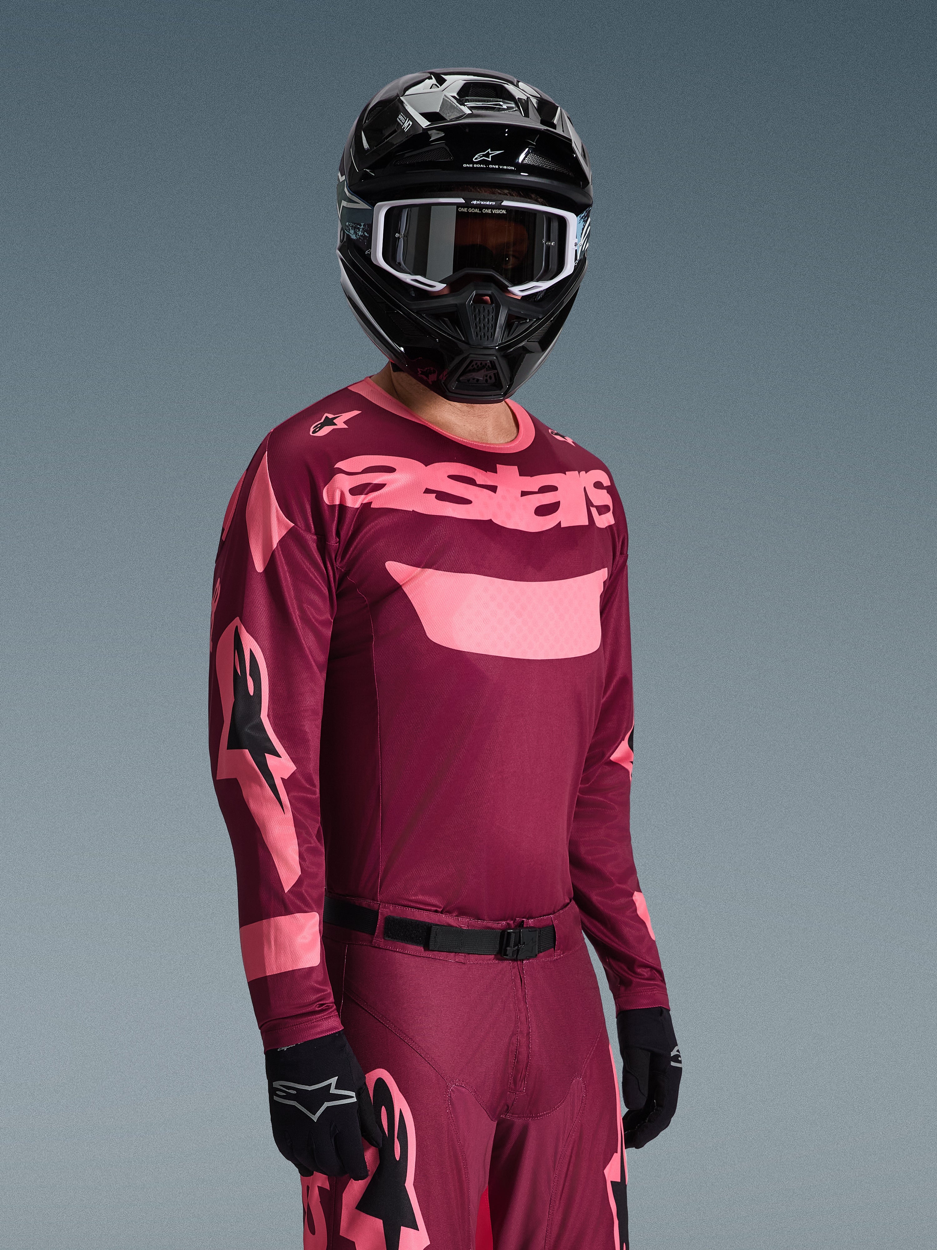 Motocross rider wearing Alpinestars 2026 Racer Riway Gear Set, Burgundy and Pink jersey with bold 'astars' branding, matching pants with pink accents, black helmet and gloves, professional racing outfit for off-road motocross