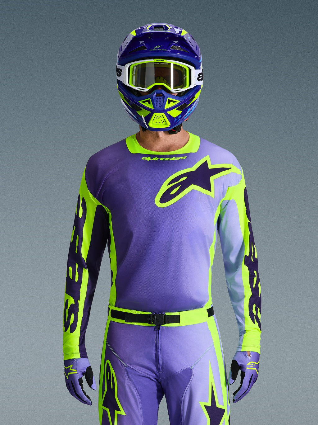Alpinestars 2026 Racer Portl Jersey, Motocross Jersey, Purple and Yellow Fluo, worn with matching motocross pants, gloves, and helmet, featuring a large Alpinestars star logo on the chest, studio shot against a gray background.