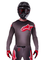 Alpinestars 2025 Supertech Lipan Jersey, Motocross Jersey, Smoke and Red, featuring a large red and white chest logo, worn with a black helmet and red and black gloves, athletic race fit with laser-cut perforations