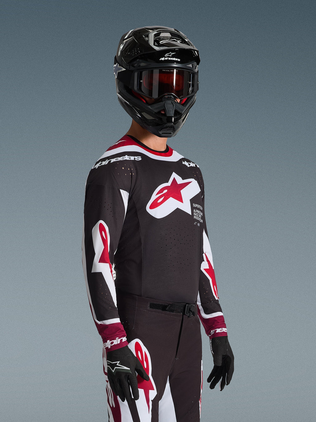 Motocross rider wearing the Alpinestars 2026 Supertech AFD Vista Jersey in Black Red and White, featuring a large red star logo on the chest and laser-cut perforations, paired with a black helmet and matching racing pants for off-road performance