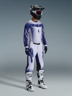 Motocross rider wearing complete professional racing gear, 2026 Supertech Scenz Jersey in light gray and dark blue, matching motocross pants with star graphics, black helmet with red goggles, white and black performance boots, coordinated blue and white gloves for off-road racing