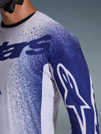 Close-up of the Alpinestars 2026 Supertech Scenz Jersey in Light Gray and Dark Blue, featuring laser-cut perforations, speckled graphic pattern, white Astars logo on the sleeve, professional motocross performance fit