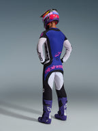 Motocross rider from behind wearing complete racing gear, featuring the 2026 Techstar Knif Jersey with a blue back and white perforated sleeves, matching black pants with pink Alpinestars branding, colorful helmet, and purple boots, coordinated outfit for off-road competition.