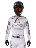 Alpinestars 2025 Racer Hollow Jersey, Motocross Jersey, White and Black, worn with matching white MX pants and a black helmet with orange goggles, featuring bold Alpinestars branding and globe graphics, professional off-road racing gear