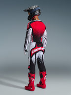 Rear view of a motocross rider wearing the Alpinestars 2026 Techstar Nomur Jersey in Black White Red, featuring a red gradient back and wavy sleeve patterns, paired with matching motocross pants, red boots, and a black helmet for a coordinated off-road racing kit