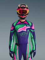 Alpinestars 2026 Techstar Nomur Gear Set, Motocross rider wearing vibrant green and purple racing jersey with pink accents, matching gear set with multi-colored helmet and goggles, high-performance off-road motorcycle outfit