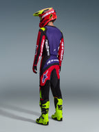 Motocross rider seen from the back wearing the Alpinestars 2026 Fluid Grid Jersey and matching pants in Red Black and Purple, accented with white branding, paired with neon yellow boots and a red and yellow helmet, complete off-road racing outfit