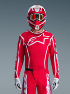Alpinestars 2026 Fluid Apex Jersey, Motocross Jersey, Red and White, worn by a rider with a matching red and white helmet and orange goggles, featuring a prominent white logo on the chest, athletic fit, part of a coordinated off-road racing gear set