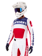 Motocross rider wearing the Alpinestars Limited Edition Techstar Fortitude Jersey, Bright Red White and Blue, featuring a white helmet with blue goggles and matching pants, high-performance racing apparel for off-road competition
