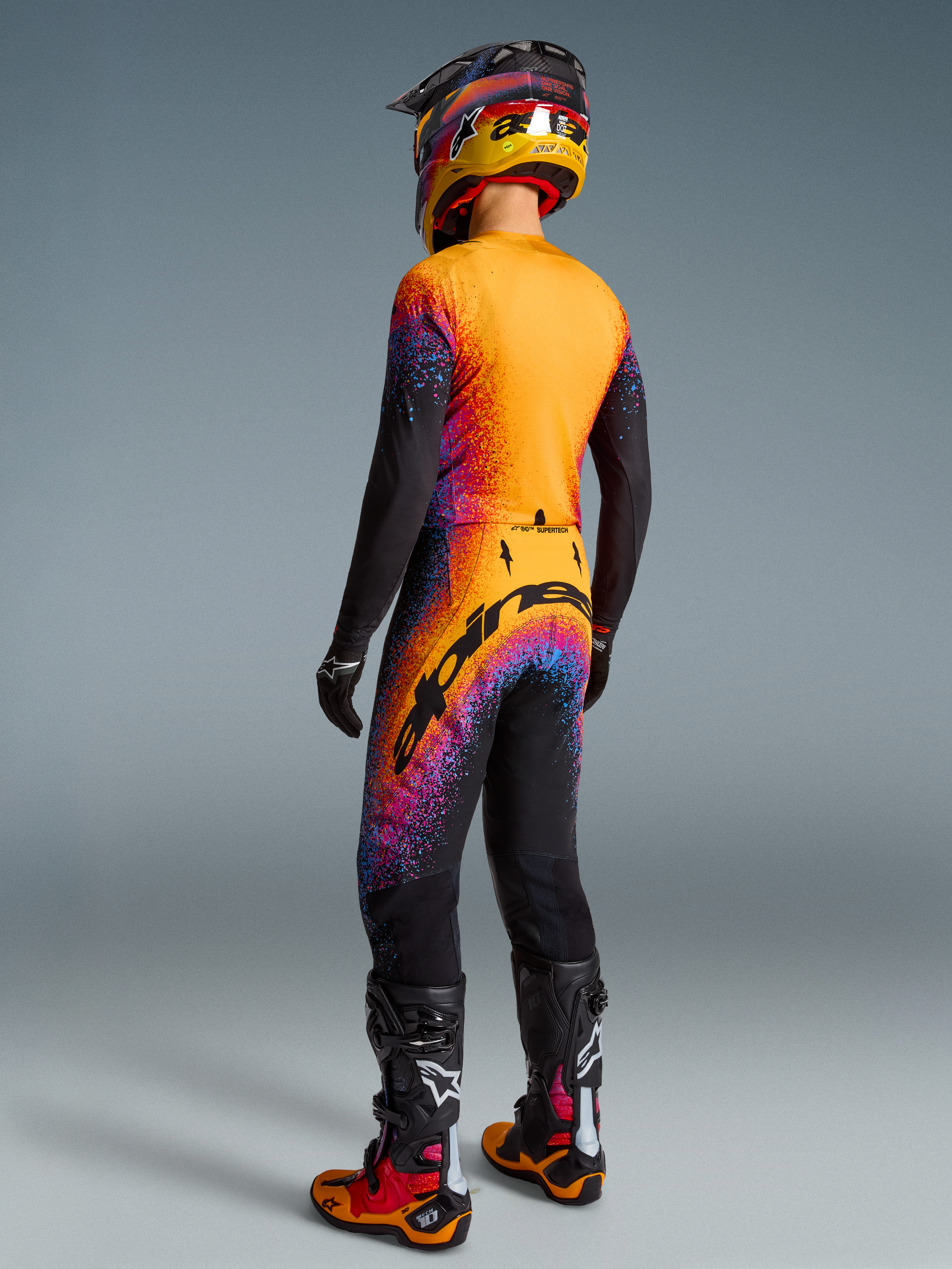 Alpinestars Supertech Black Hole Motocross Gear Set, black and orange with purple cosmic graphics, male rider back view.