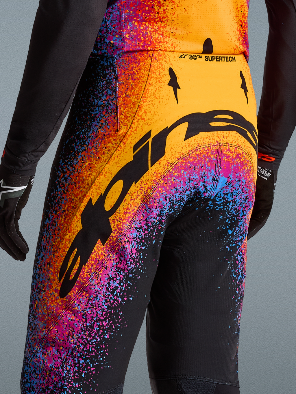 Alpinestars Limited Edition Supertech Black Hole Motocross Pants, black with orange and purple cosmic splatter graphics.