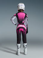 Alpinestars 2026 Stella Techstar Nomur Gear Set, female motocross rider viewed from behind, pink and black jersey with white striped sleeves and speckled pattern, matching pants with white Alpinestars logo, white helmet and white off-road boots