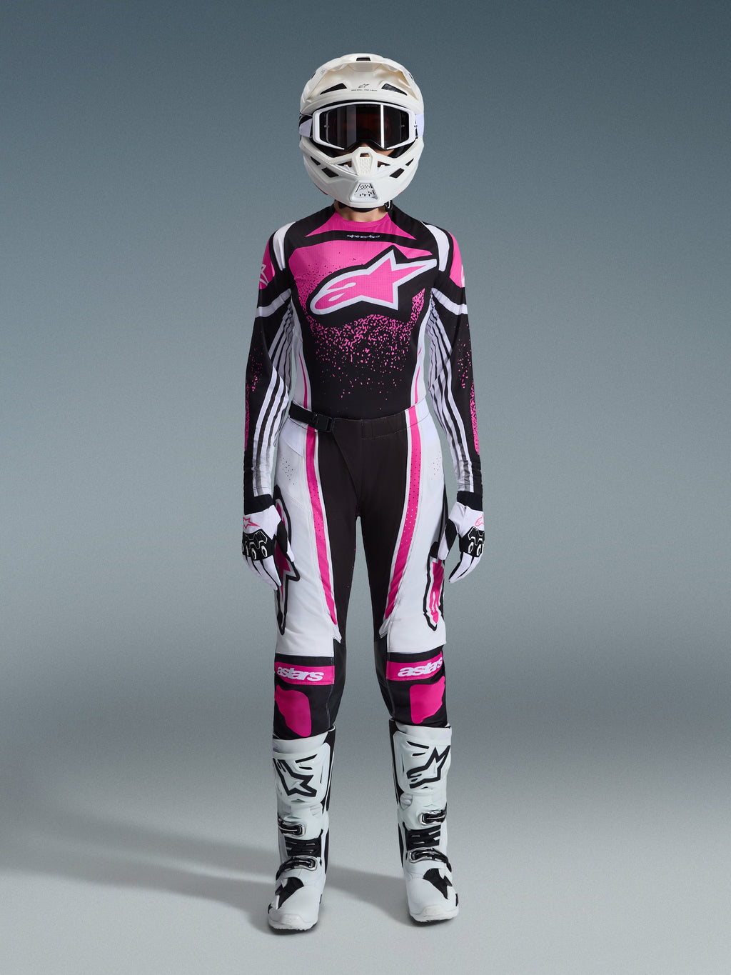 Alpinestars 2026 Woman Stella Techstar Nomur Gear Set, full motocross racing outfit in Black White and Fuchsia, jersey featuring a large star logo and pink splash design, matching pants, white helmet with goggles, black and white boots, coordinated women's off-road gear
