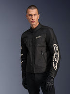 Alpinestars T-Dyno Air Jacket in Black, male model wearing a vintage-inspired textile motorcycle jacket with mesh panels for ventilation, large white Alpinestars logo on sleeves, paired with black riding gloves, urban motorcycle gear design
