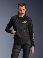 Alpinestars Stella T-Dyno Air Jacket, Women's Motorcycle Jacket, Black with white logos, worn by a female rider with braided hair, featuring breathable 3D mesh panels and zippered pockets, paired with black textured riding pants, vintage-inspired urban riding gear