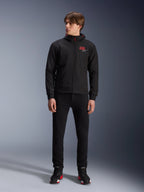 Alpinestars MM93 Radium Tech Hoodie, black urban motorcycle hoodie, featuring a red 93 logo and white star logo on the chest, worn by a model with black pants and matching riding shoes, sleek windproof technical shell for urban riding.