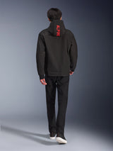 Alpinestars Radium Tech Hoodie, urban motorcycle jacket, Black, back view featuring bright red 'ALPINE' text on the hood, worn with black pants and sneakers, sleek technical shell for commuting.