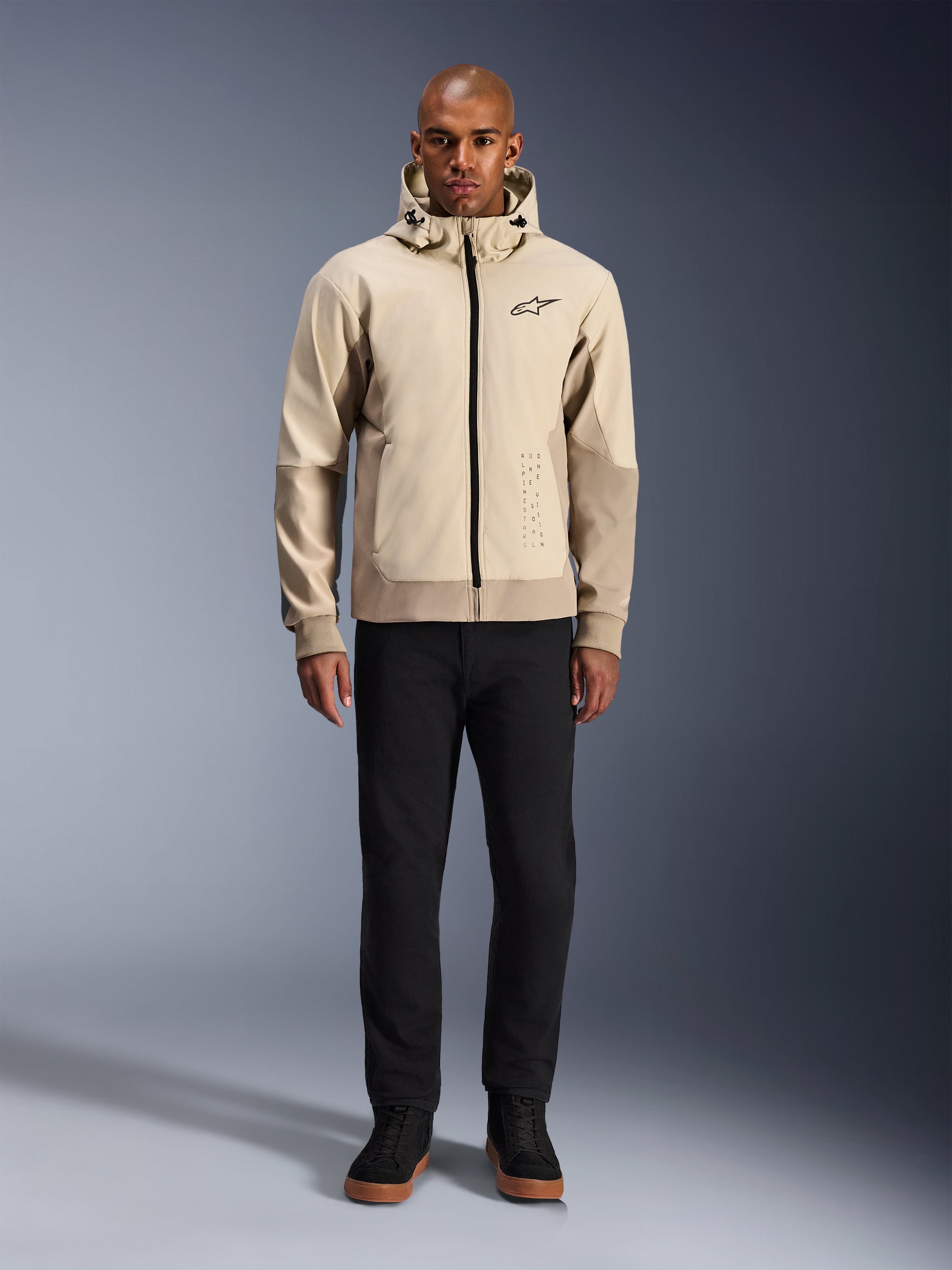 Alpinestars Radium Tech Hoodie in Mastic Aluminum, urban motorcycle hoodie worn by a male model with black pants and black boots, featuring a full-length black zipper, small chest logo, and athletic fit for city riding.