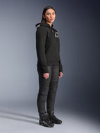 Woman wearing Alpinestars Stella Chrome V2 Sport Hoodie in black, featuring white Alpinestars branding, paired with black motorcycle riding pants and boots, urban riding gear for women with a casual athletic fit