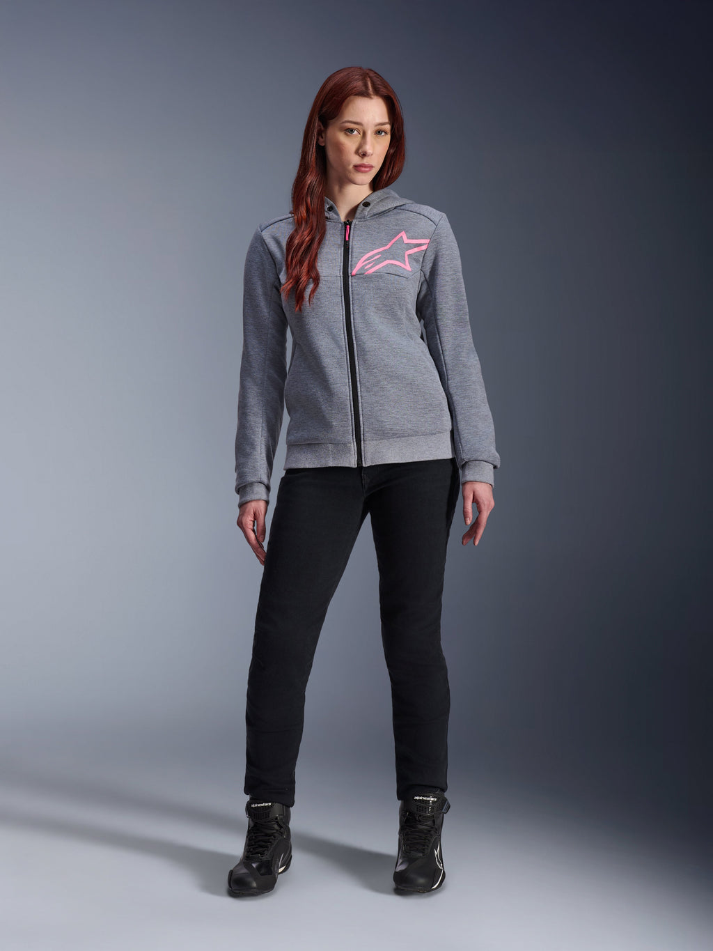 Alpinestars Stella Chrome V2 Sport Hoodie, Gray Heather Pink Fluo, worn by a woman with black pants and boots, featuring a pink Alpinestars star logo on the chest, full-zip urban motorcycle gear, lightweight tech fleece with a casual athletic fit.
