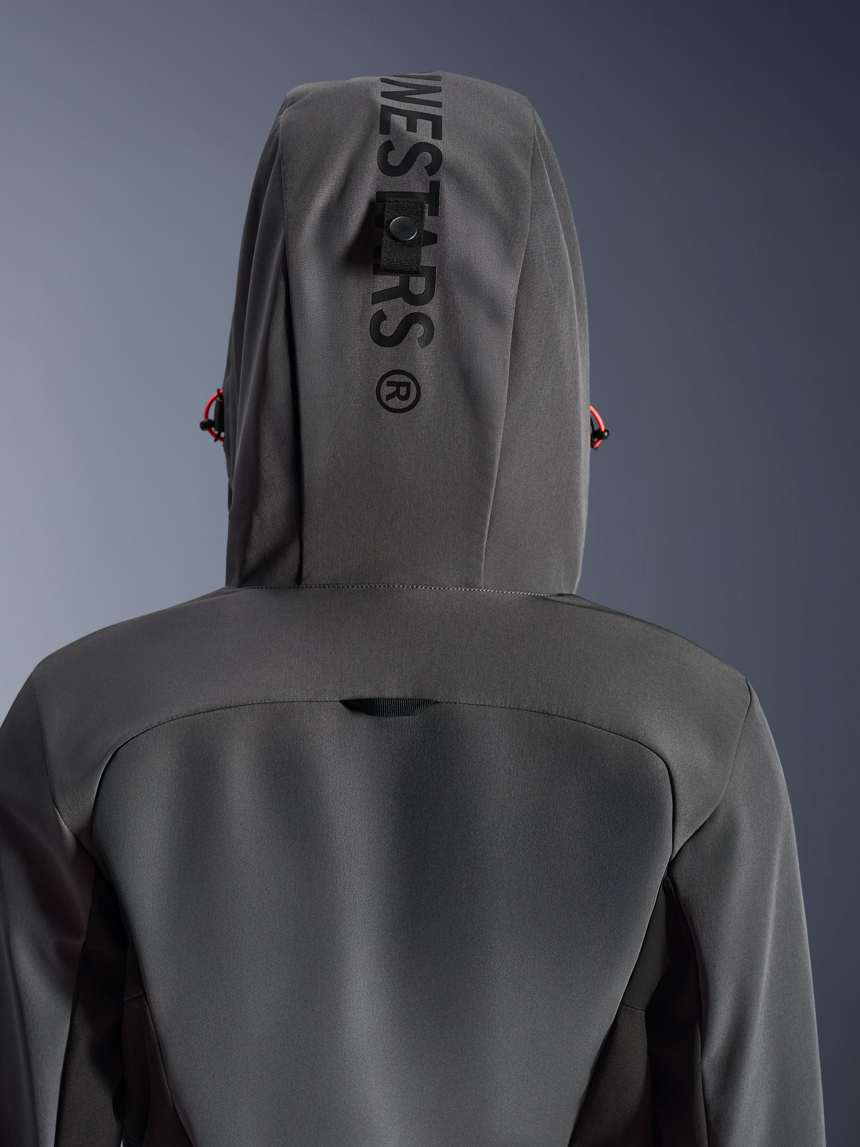 Alpinestars Woman Stella Radium Tech Hoodie, Deep Gray Black, close-up back view showing the hood with vertical branding and management loop, red drawstring accents, durable 3-layer windproof textile construction for urban motorcycle riding.
