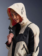 Alpinestars Molly Air Jacket in Black Almond, worn by a female model with the hood up, featuring cream and black color-blocking, a vibrant orange mesh lining, and technical urban design elements including a star logo and zip details.